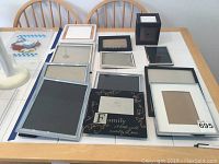 12 assorted photo frames in various sizes and 1 black photo box displayed on a table.
