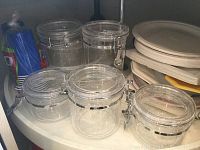 Photo showing six clear plastic canisters with locking lids, blue disposable cups in plastic wrap, stacked plastic plates and dishes.