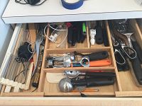 Wide view of wooden drawer organizer filled with kitchen utensils including scissors, knives, can openers, peelers, and corkscrew