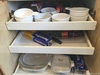 Image showing a lower drawer with two Corning Ware casserole dishes with lids and aluminum foil box underneath the drawer with ramekins.