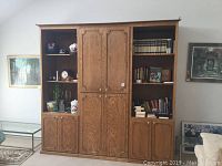 Front view of wooden entertainment center showing central paneled doors and side shelving units with various items