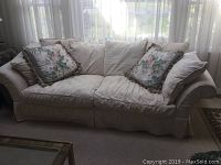 Full view of light beige couch with two floral throw pillows and visible minor soiling on fabric.