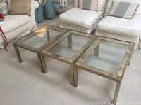 Three small rectangular coffee tables with glass tops and bronze metal frames nested together on a carpeted floor.