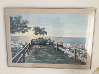 Photo of one framed picture showing scenic wooden deck with metal table and chairs overlooking water, surrounded by trees and flowers.