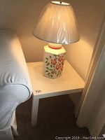 White square side table with a decorative floral lamp on top, positioned next to a white sofa.