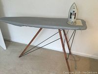 Full view of the wooden ironing board with grey cover and Norelco iron placed on top.