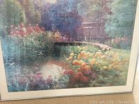 Large framed floral-themed picture showing a garden scene with a bridge and colorful flowers.