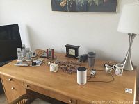 Wide angle of all items on wooden desk, showing phone system, clock, reading glasses, Alexa, cups, staplers, and lamp