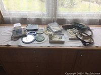 Lot displayed on cabinet with items well spread: blood pressure monitor with cuff, costume pearl necklaces in display cases, small mirror, and leather belts.