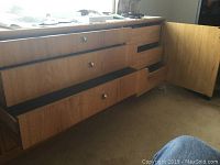 Light wood low dresser showing four drawers with metal round knobs and a side cabinet door open, exposing two shelves. Wear visible on top surface.
