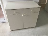 Front view of small white chest of drawers and cabinets showing two drawers on top and two doors.