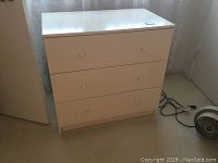 White 3-drawer chest of drawers photographed from a frontal angle showing drawer knobs and overall condition.