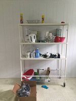Full metal shelving unit on wheels against a white paneled wall, showing three solid shelves and wire basket at base. Various items placed on shelves but not included in sale.
