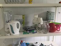 Shelf with white Hamilton Beach blender, Proctor Silex electric kettle, white salad shooter, multiple glass vases, red teapot with broken lid handle, corkscrew set, and large white serving bowl visible.