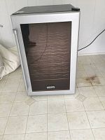 Front view of the Koldfront wine fridge with glass door closed, showing the full unit and part of the floor where it stands.