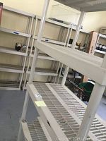 Three white plastic shelving units assembled in garage. Shelves have grid open design and vertical supports.