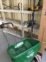 Shows Scotts Turf Builder spreader with green plastic hopper and metal frame