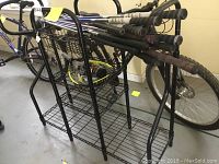 Photo showing black metal storage rack holding multiple golf clubs with black and grey grips, with a bicycle in the background.