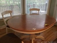 Photo of the wood oval pedestal dining table with four chairs around it, showing the wood top and white pedestal base