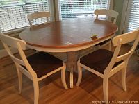 Four white wooden dining chairs with brown upholstered seats arranged around a round dining table.