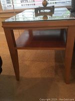 Front view of one end table showing glass top, open shelf, tapered legs