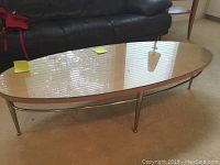 Front view of oval glass top coffee table with light wood rim and silver metal legs