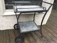 Side angle of patio tea cart showing curved metal frame, wheels, and two stone-patterned shelves