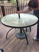 Round outdoor patio table with glass top and metal legs, held by person demonstrating size and condition.