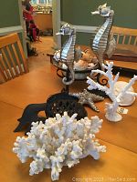 Two metal silver-tone seahorses on stands, large white coral pieces, metal starfish, black decorative fish on wooden table.