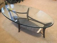 Clear oval glass coffee table with metal legs and lower shelf viewed from front.