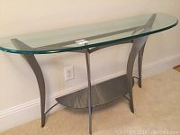 Front view of the metal and glass console table showing the curved metal legs and the clear glass top.