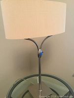 Close view of matching table lamp with oval beige shade and metal stand on glass table.