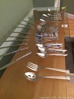 Full spread of stainless steel flatware pieces for 10 place settings, forks, spoons, knives, and serving pieces laid out on table.