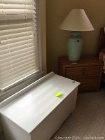 White wooden storage bench with smooth finish and hinged lid near window and nightstand.