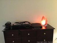 Photo of all items on top of a dark wood dresser including massagers and salt lamp