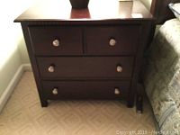 Front view of the bedside table showing four drawers and silver knobs, with scratches and water marks on the top surface.