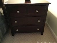 Front view of the dark brown wooden bedside table with four drawers and clear round knobs.