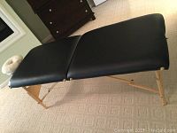 Side profile view of black padded massage table with wooden legs and metal braces