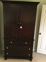 Full front view of dark wood armoire showing upper cabinet doors and four drawers below with silver knobs.