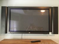 Front view of HP 42in wall-mounted TV with side speakers and remote below