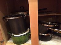 Photo shows several pots and pans stacked inside a kitchen cabinet including a green cast iron Dutch oven.