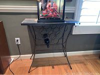 Full view of black metal wine rack table with circular bottle holders and slate top, containing one wine bottle.
