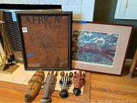 Wide view showing all items: two framed African themed wall arts and four wooden animal masks on floor.