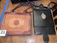 Two handmade leather handbags placed side by side on wooden surface, showing front designs.