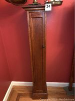 Full view of the tall wooden cabinet standing on the floor against a red wall, showing its size and color