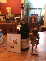 Overall lot view showing magnum bottle, framed wall art, and paper figurine on table