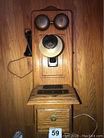 Front view of vintage wall phone showing oak body, brass bells, ivory and black mouthpiece, and black handset on side