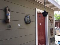Wall showing the wood carved lion wall art, the wind chimes on driftwood, and the red door with the lantern above it.