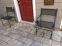 Two black wrought iron garden chairs on stone patio near red door, with coyote statue.