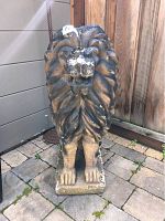 Front view of the cement lion statue on stone pavers with some paint marks visible on the lion's face and mane.